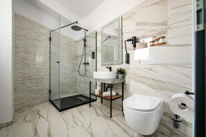 Un bagno moderno con cabina doccia in vetro, pavimento in marmo, un water bianco e un lavandino con uno specchio sopra.