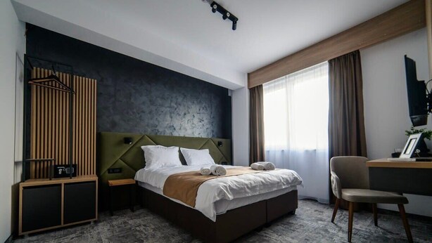 Une chambre d’hôtel avec un lit, un bureau, une chaise, une armoire et une grande fenêtre.