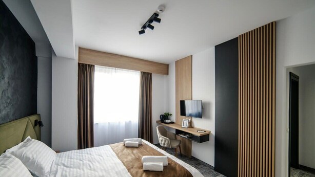 A hotel room with a bed, a desk, a chair, a television, and a large window with curtains.