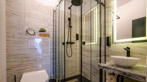 A modern bathroom with a glass-enclosed shower, a white toilet, a marble countertop, and a large mirror.