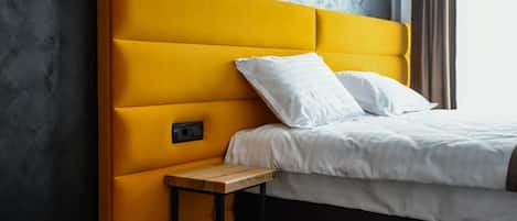 A bed with a yellow headboard, white bedding, and a small wooden nightstand.
