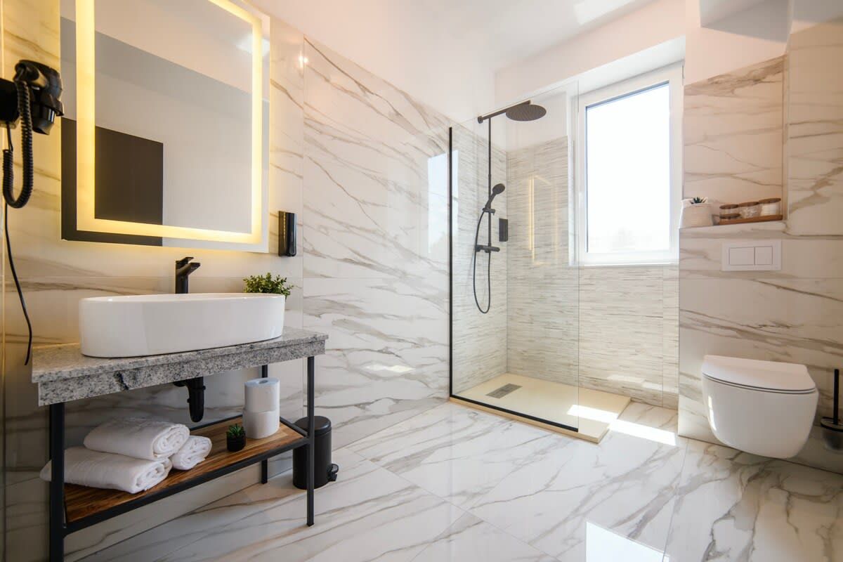 A modern bathroom with a marble floor, a glass-enclosed shower, a white sink, and a large mirror.