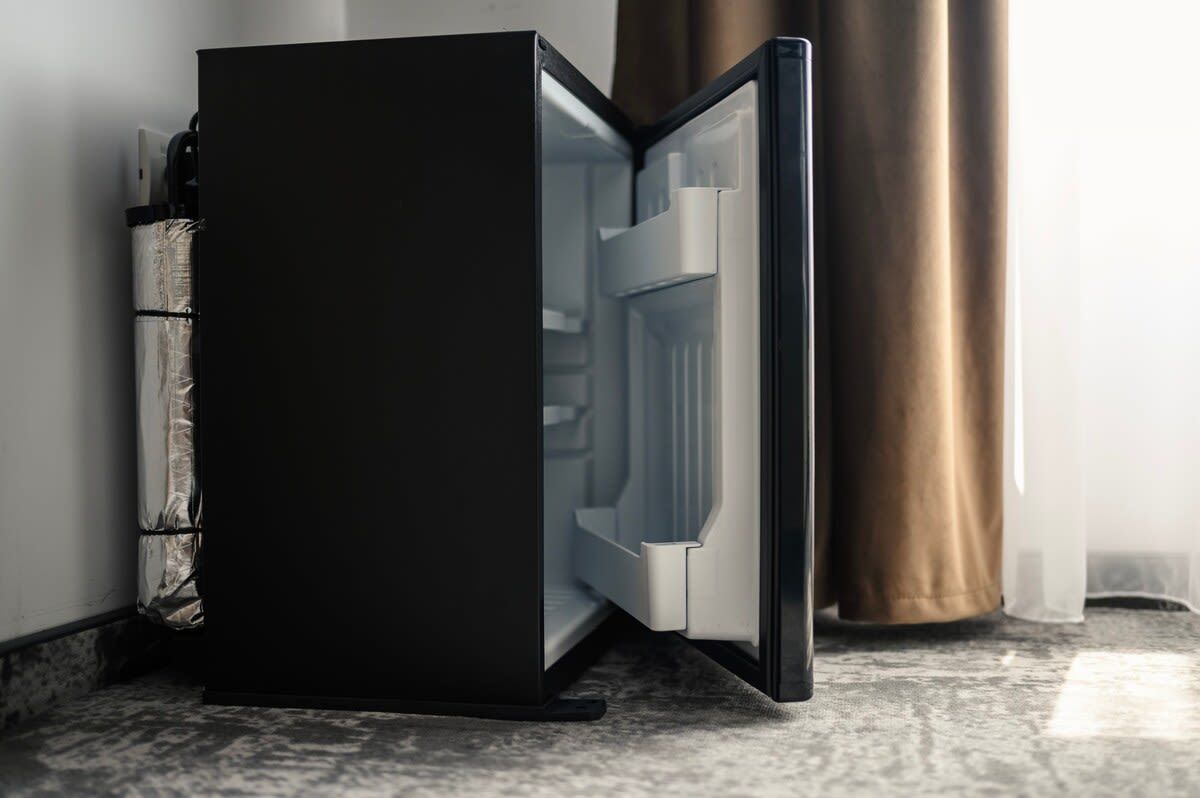 A modern, black-framed refrigerator with a metallic handle, positioned against a wall with a metallic curtain.