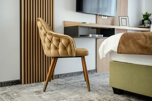 A modern bedroom with a tufted headboard chair, a bed with a white and brown blanket, and a television mounted on the wall. - GBU Home Timisoara Olive 407 (Timișoara)