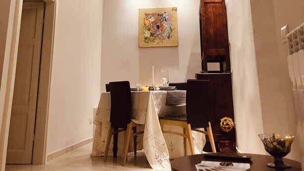 A dining area with a table set for two, a wooden chair, a small table with a bowl, and a painting on the wall. - I Borghi della Maddalena (Borgo a Mozzano)