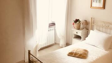 Une chambre à coucher avec un lit, une table de chevet, une lampe, un tableau encadré et une fenêtre avec des rideaux.