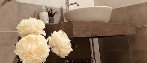 Un baño moderno con un espejo grande, un lavabo y una bañera. Hay flores blancas en un jarrón y una toalla amarilla en un estante.