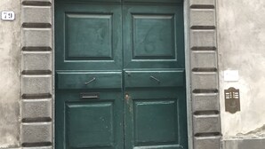A green double door with a metal grille, set in a stone wall with a number '79' visible. - I Borghi della Maddalena (Borgo a Mozzano)