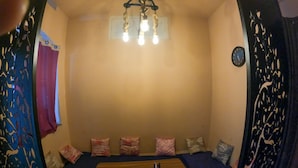 A cozy room with a wooden table, a sofa with cushions, a decorative wall hanging, and a ceiling light fixture. - Jungle by sturmfrei Gokarna (Kumta)