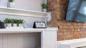 Una estantería blanca con plantas en macetas, un calendario y un televisor de pantalla plana montado sobre una pared de ladrillo.