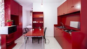 A compact kitchen with red cabinetry, a dining table with chairs, and a small seating area.