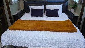 A bed with a white quilt, two dark pillows, and a brown throw blanket. - Reconnect with nature at this unforgettable escape (O'Brien)