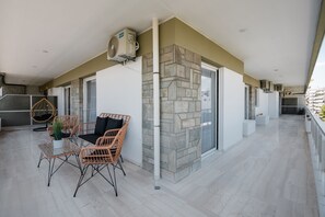 Un balcón espacioso con pared de piedra, mobiliario de mimbre y una mesa de vidrio.