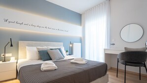 Une chambre moderne comprenant un lit, une table de chevet, une chaise, un bureau et un mur orné d’une citation.