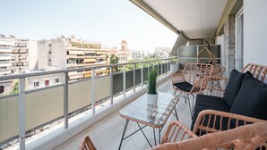 Un balcon agrémenté de meubles en osier, d’une plante en pot et offrant une vue sur le paysage urbain.