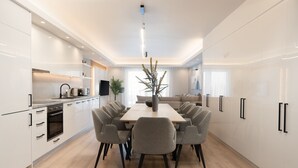 Une cuisine moderne avec des meubles blancs, un îlot central et un coin repas doté de chaises grises.