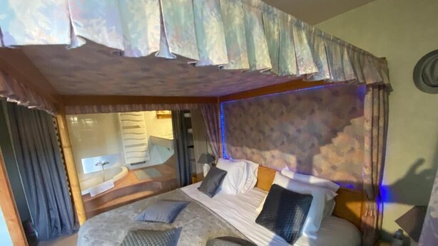 Une chambre à coucher avec un grand lit, une tête de lit ornée d’un motif et une table de chevet avec une lampe.
