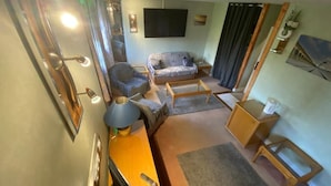 Un salon de taille réduite comprenant un canapé, des fauteuils, une table basse, un téléviseur et une petite table d’appoint.