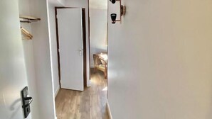 Un couloir étroit doté d’un plancher en bois, de murs blancs et d’une porte donnant sur une autre pièce.