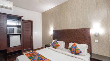 A hotel room with a bed, a small refrigerator, a wooden wardrobe, and a tiled wall.