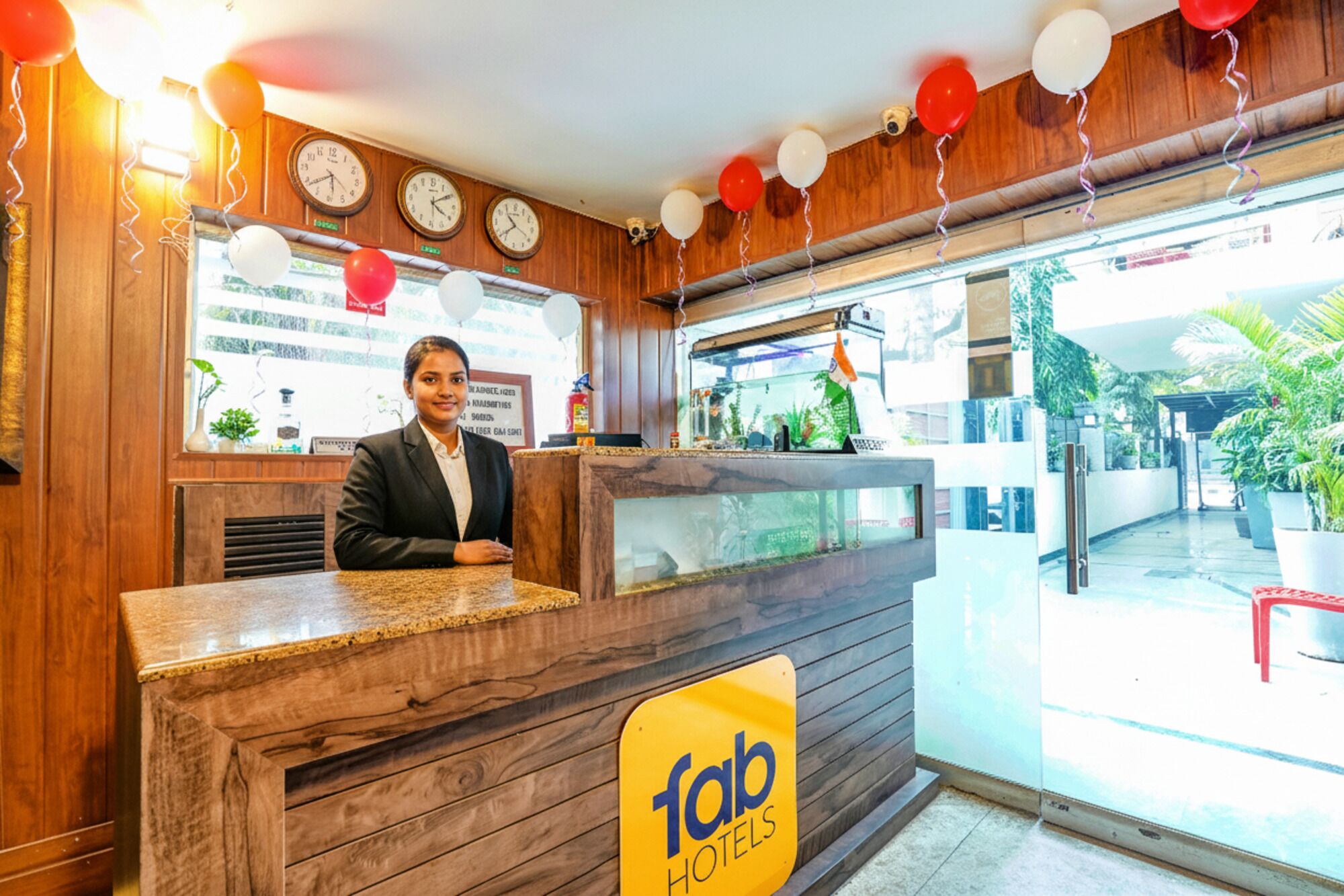 A hotel reception desk with clocks, a sign for 'fab hotels', and a view of the outside.