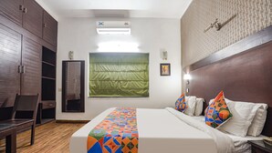 Ein Hotelzimmer mit Bett, Sessel, Kleiderschrank, einem Fenster mit grünem Vorhang und einer Wand-Klimaanlage.