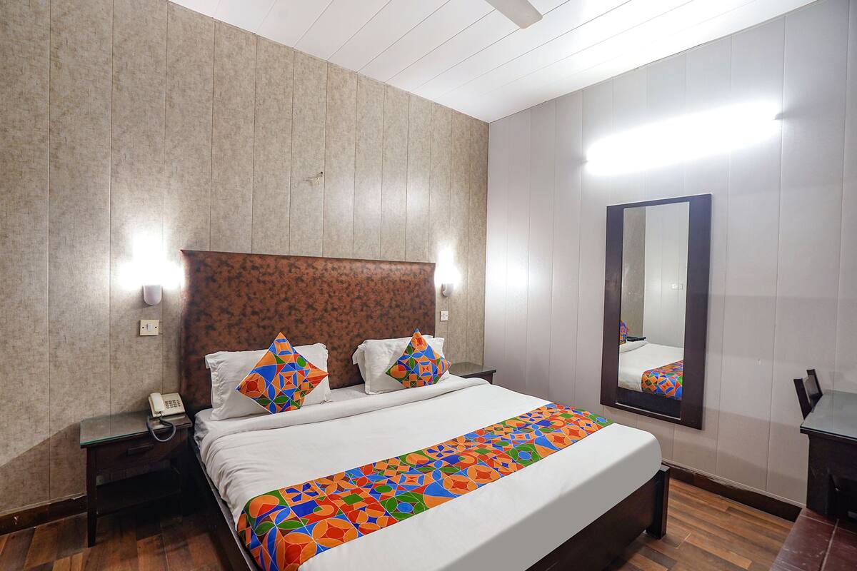 Quarto de hotel com uma cama grande, mesa de cabeceira com telefone, espelho e piso de madeira.