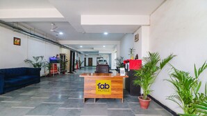 A hotel reception area with a reception desk labeled "fab hotels," a blue sofa, and potted plants. - Fabexpress Abode Inn (New Delhi)