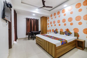 A hotel room with a bed, a desk, a chair, a wardrobe, and a ceiling fan. - Fabexpress Abode Inn (New Delhi)