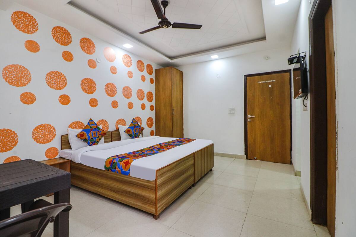 A bedroom with a bed, wooden wardrobe, ceiling fan, and a wall with orange circular patterns.