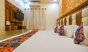 A hotel room with a wooden wall, a flat-screen TV, a patterned carpet, and a row of pillows with colorful patterns.