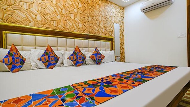 Quarto de hotel com parede estampada, cama com roupa de cama branca e almofadas coloridas.