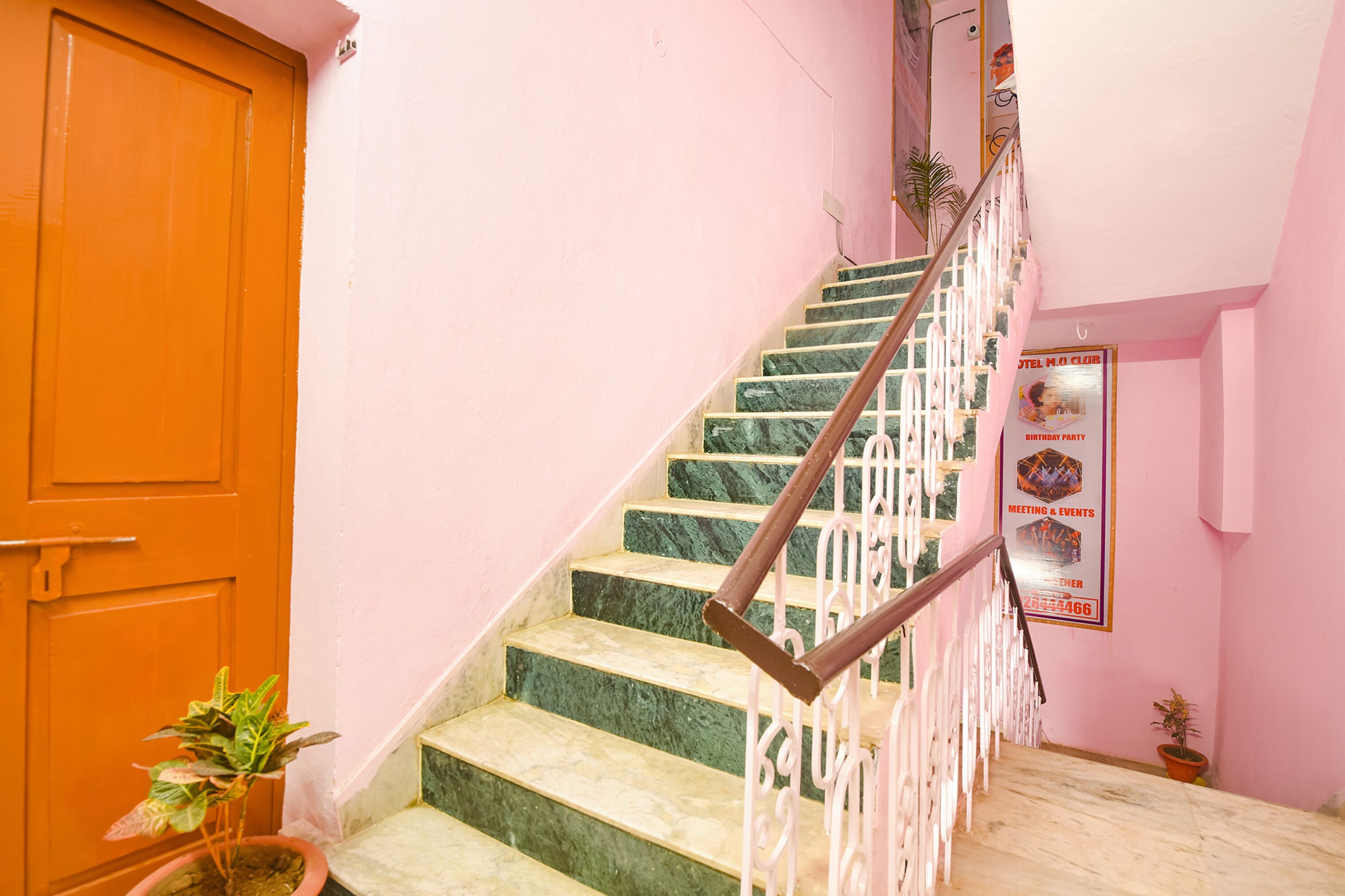Una escalera con escalones de mármol y barandilla de madera que conduce a una habitación con pared rosa y puerta de madera.
