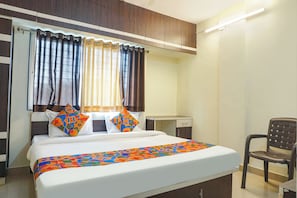 A hotel room with a bed, a chair, a desk, and curtains. - FabExpress The Guest House (Pune)