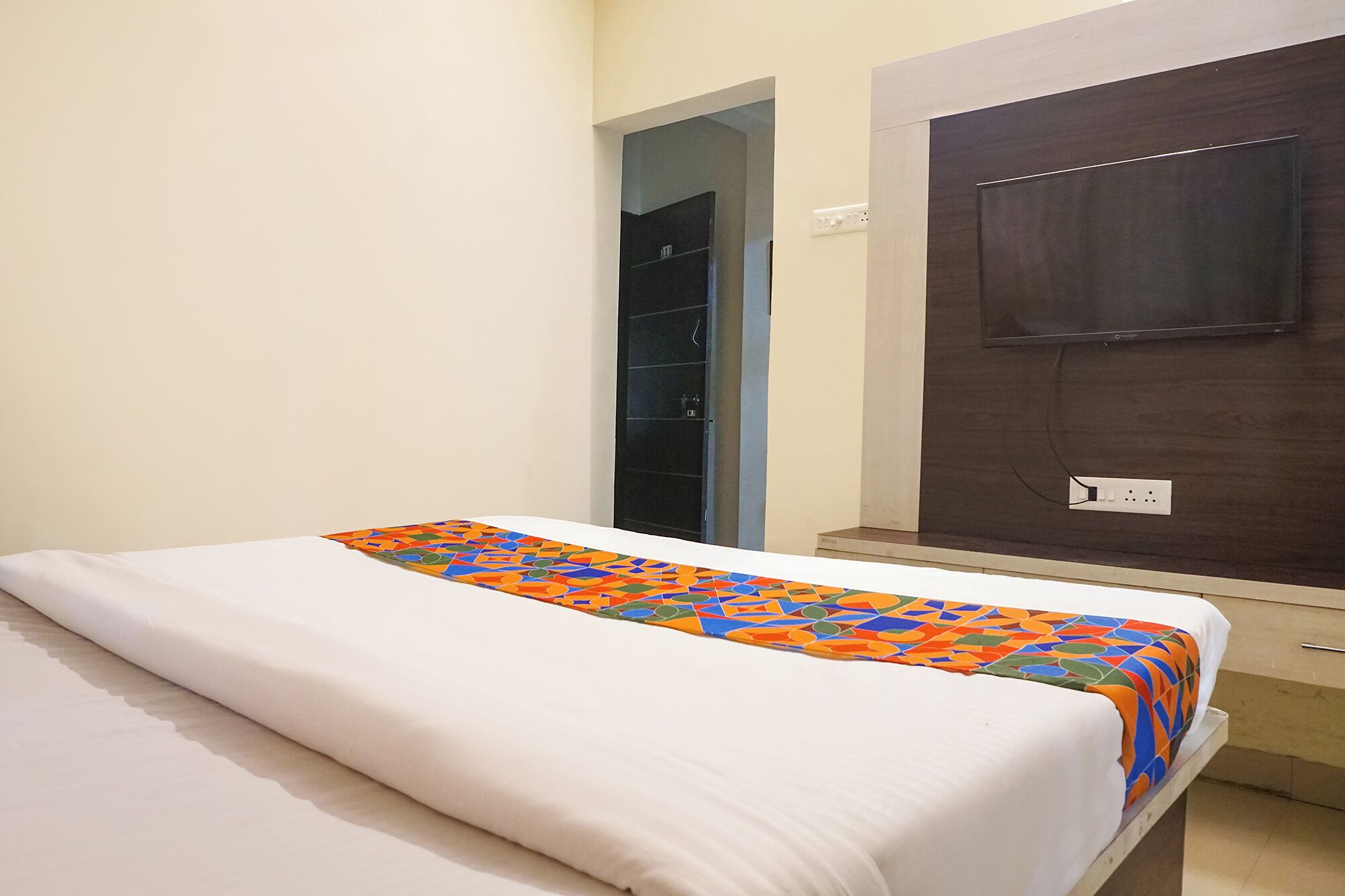 A hotel room with a bed, a door, and a wall-mounted TV.