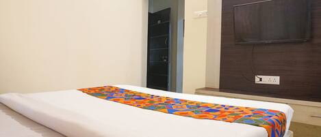 A hotel room with a bed, a door, and a wall-mounted TV.