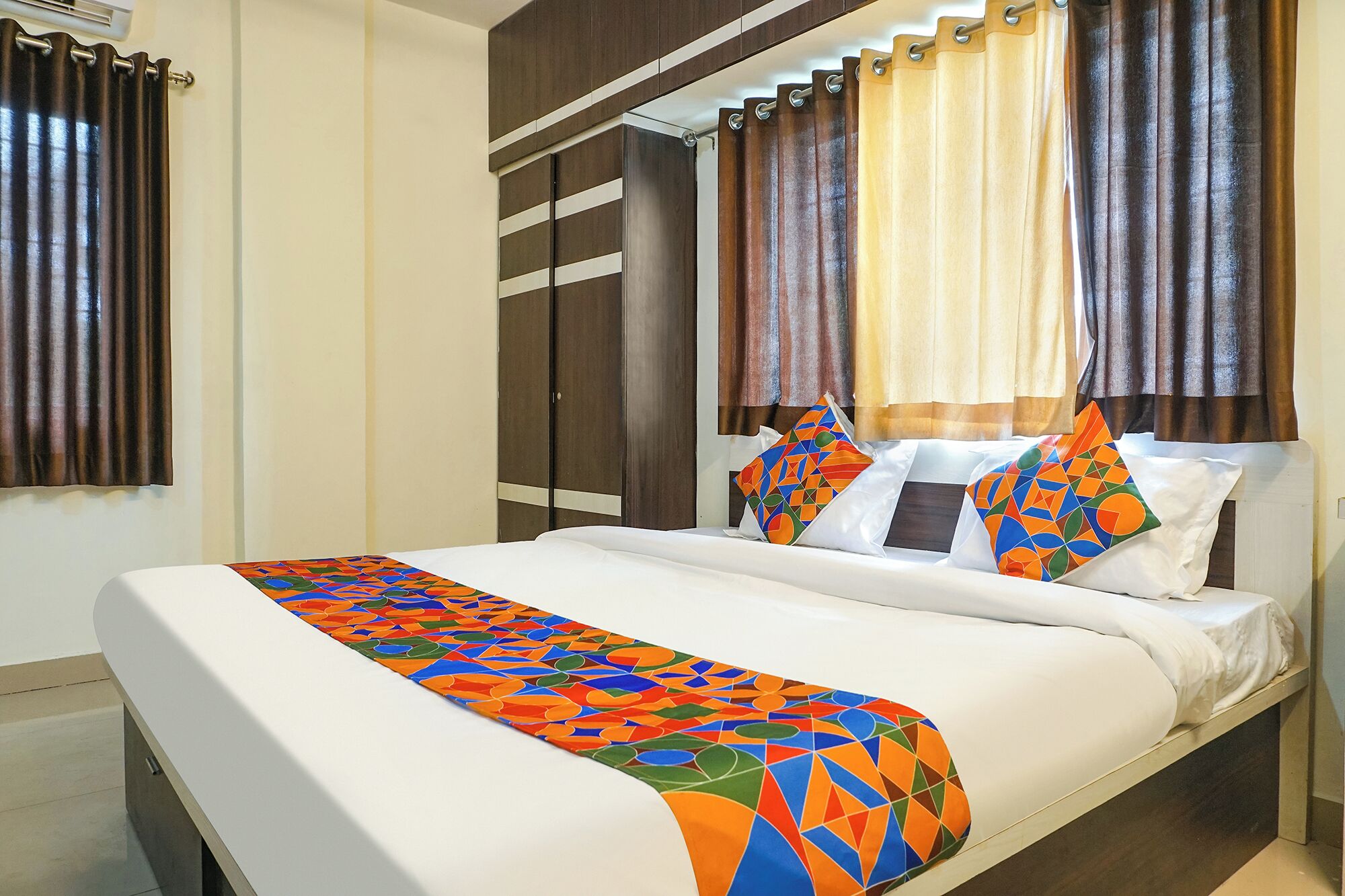 A hotel room with a bed, curtains, and a colorful geometric throw blanket.