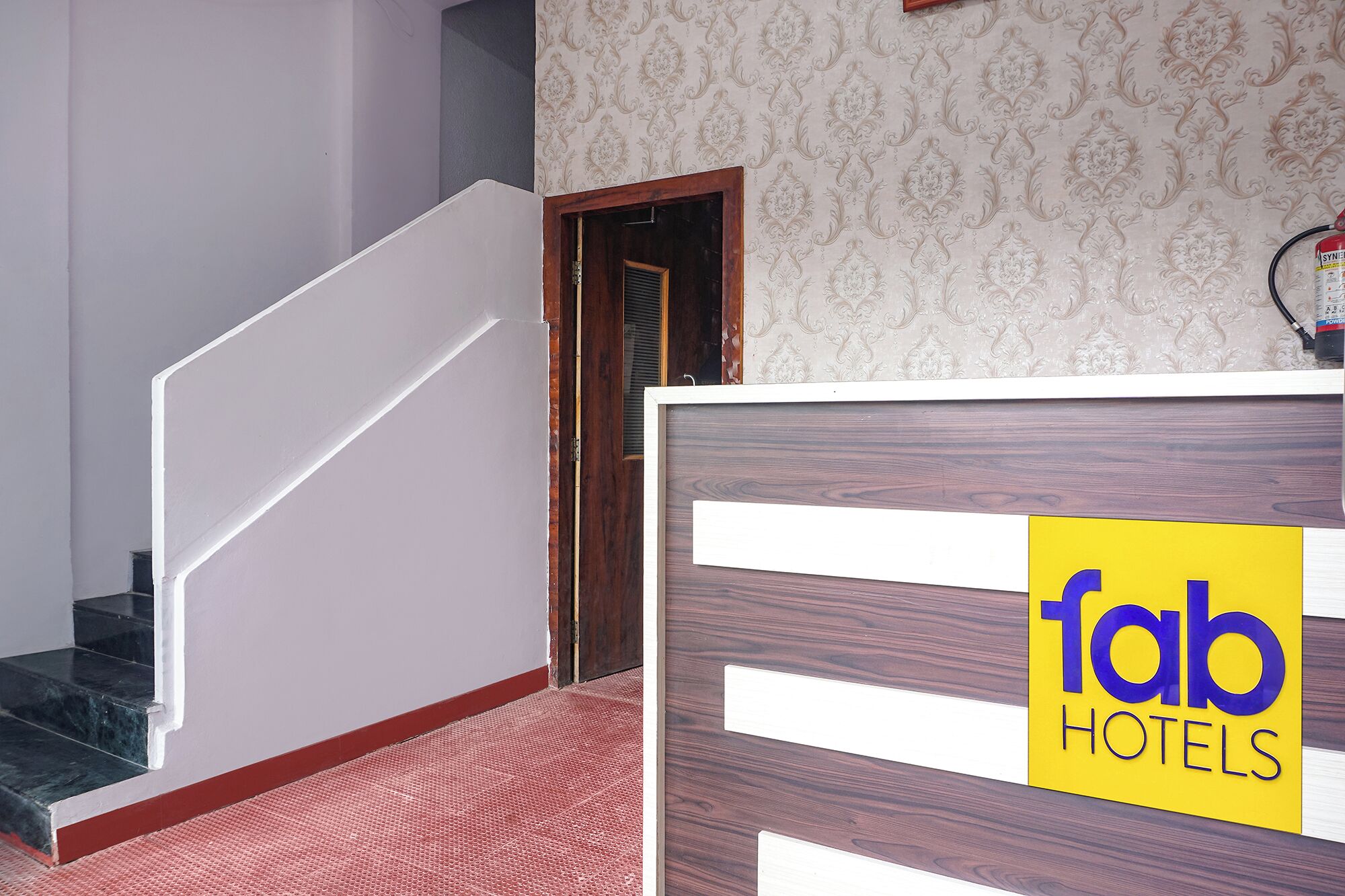 A hotel reception desk with a sign reading 'fab hotels' and a staircase leading to an upper floor.
