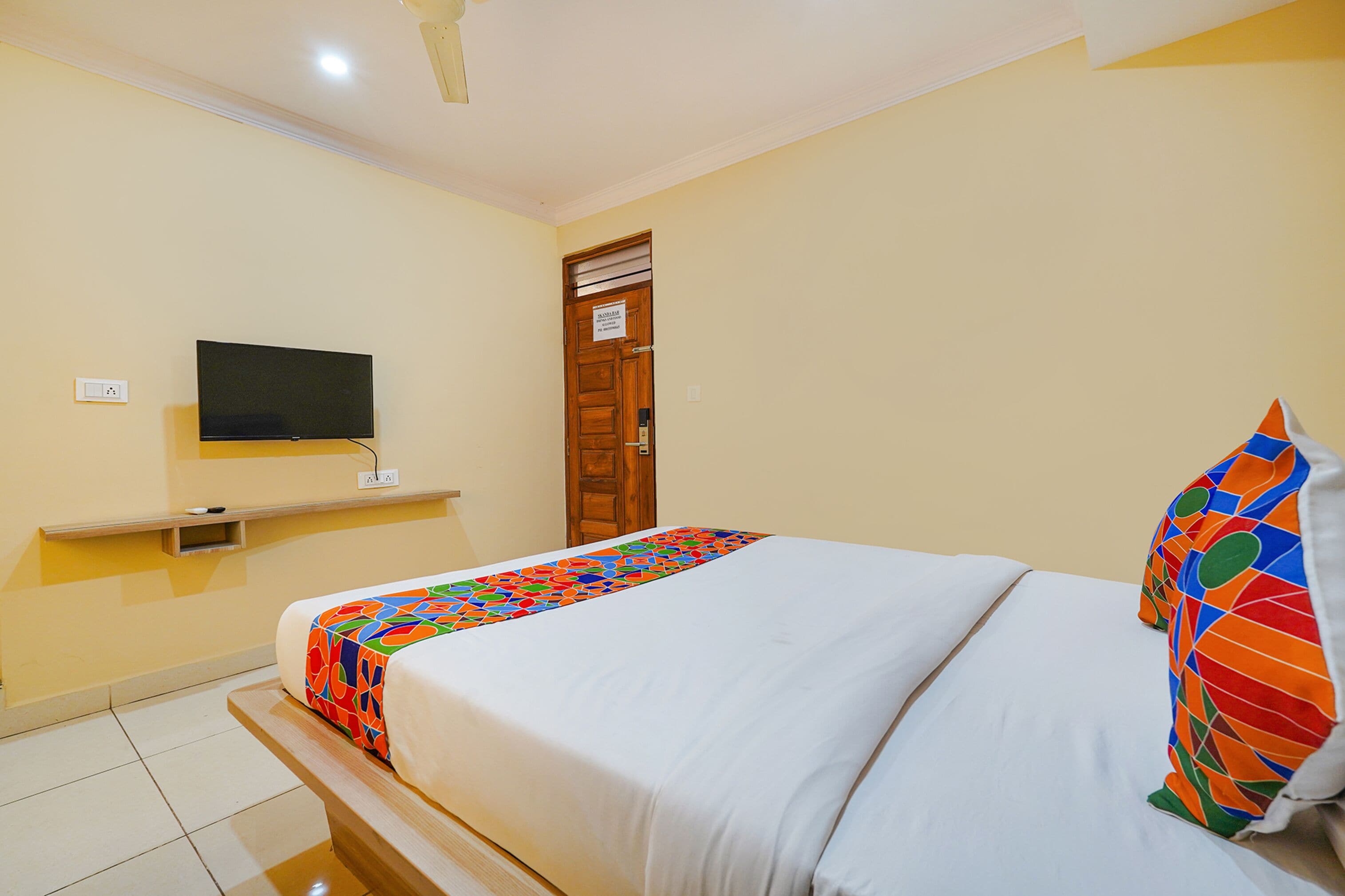 A hotel room with a bed, a TV mounted on the wall, and a door with a sign.