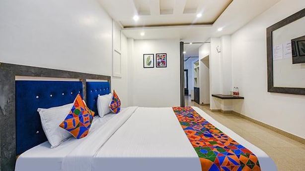 Una habitación de hotel con una cama grande, un cabecero y una colcha colorida. Hay una mesita con un espejo y un cuadro enmarcado en la pared.