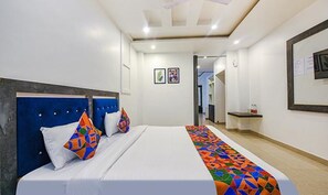 A hotel room with a large bed, a headboard, and a colorful bedspread. There is a small table with a mirror and a framed picture on the wall. - Fabhotel The Micky House (Kasauli)