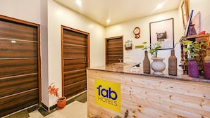 Un mostrador de recepción con acabado de madera y un cartel que dice 'fab hotels'. Hay puertas de madera y un reloj en la pared.