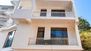 Un edificio de varios pisos con un letrero que dice 'Fab Hotels'. Cuenta con una zona de estacionamiento techada donde se ven coches y una motocicleta.