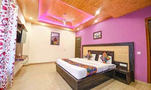 A bedroom with a wooden ceiling, a bed with colorful bedding, a nightstand, and a wall-mounted TV. - Fabhotel The Kasauli Heavens (Kasauli)