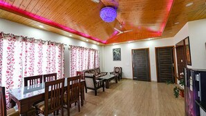 Un comedor con mesas y sillas de madera, un ventilador de techo y cortinas con motivos florales.