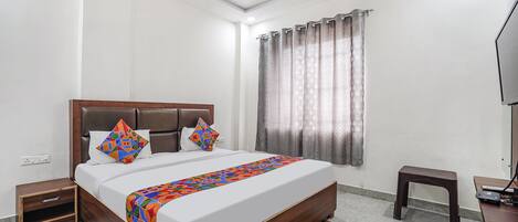 A bedroom with a large bed, a wooden headboard, a nightstand, a small stool, a television, and a window with curtains.