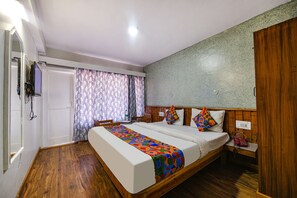 A double bed with a colorful blanket, a wooden headboard, a bedside table with a phone, and a window with patterned curtains. - Fabhotel Monalisa (Manali)