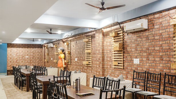 Un'area pranzo con pareti in mattoni, ventilatori a soffitto e un manichino. Tavoli e sedie disposti per i commensali.