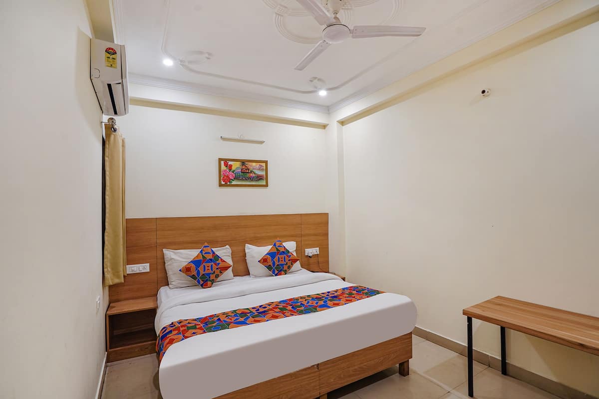 Quarto com cama, mesa de cabeceira, ventilador de teto, aparelho de ar condicionado e um pequeno banco.