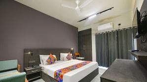 A modern hotel room with a large bed, a desk, a chair, a nightstand, and a ceiling fan. - Fabhotel Naina Residency (Rishikesh)